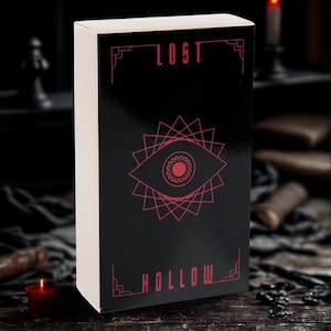 May include: A rectangular box with a black front panel and white sides. The front features the red text LOST at the top and HOLLOW at the bottom, with a central red graphic of an eye surrounded by geometric lines and a decorative border.