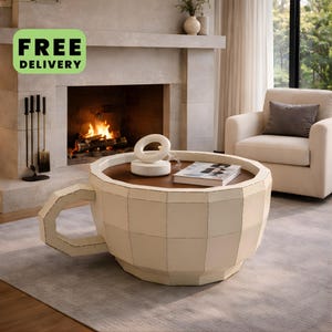 May include: A coffee table shaped like a large, faceted teacup with a cream-coloured metal exterior and a dark brown circular tabletop. The table features a prominent side handle and a smooth, flat surface, providing a unique focal point for a room.