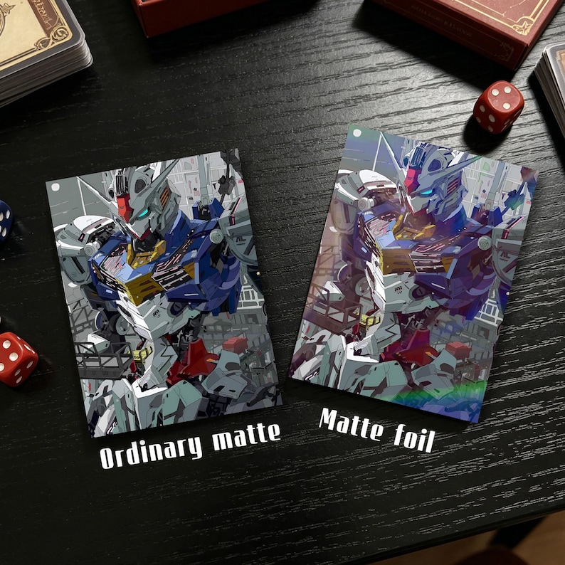 Op de afbeelding: Twee ruilkaarten met een robotillustratie in blauw, wit en rood. E&eacute;n kaart is gelabeld met "Ordinary matte", de andere met "Matte foil". Ze liggen op een donkere ondergrond met dobbelstenen en een kaartenbox.