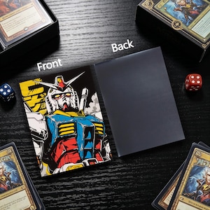 May include: Card sleeve featuring a colorful illustration of a robot with a white face, blue and red accents, and yellow details. The back of the sleeve is solid black. Dice and card boxes are in the background.