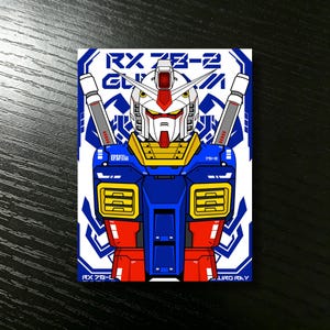 May include: A rectangular sticker featuring a stylized illustration of the RX-78-2 Gundam. The robot is depicted in a bold, colorful design with blue, red, yellow, and white accents. The sticker includes the text "RX 78-2" and "EFSF".