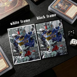 Op de afbeelding: Twee ingelijste kunstdrukken van een robot, &eacute;&eacute;n met een witte lijst en de andere met een zwarte lijst. De robot is voornamelijk blauw, wit, rood en geel. De tekst "white frame" en "black frame" staat boven de prints. Dobbelstenen en kaarthouders zijn ook zichtbaar.