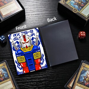 May include: A card sleeve featuring a blue, red, and yellow robot design with the text "RX 78-2". The back of the sleeve is solid black. Dice and card boxes are in the background.