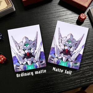 Op de afbeelding: Twee kaarthoezen met een gedetailleerde illustratie van een robot in wit, blauw en paars. E&eacute;n hoes is gemarkeerd met "Ordinary matte" en de andere met "Matte foil".