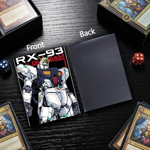 Puede incluir: Una funda de carta negra con una ilustraci&oacute;n en blanco y negro de un robot Gundam con el texto "RX-93 GUNDAM". La parte posterior es de color negro liso. Dados y cajas de cartas en el fondo.