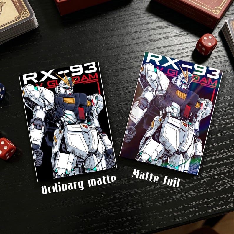 Puede incluir: Dos tarjetas rectangulares con una ilustraci&oacute;n de robot y el texto "RX-93 GUNDAM". Una tarjeta dice "Ordinary matte" y la otra "Matte foil". El robot es blanco, negro y rojo. Dados y una caja de cartas en el fondo.