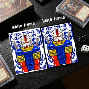 May include: Two art prints featuring a blue, red, yellow, and white robot design. The prints are labeled "RX 78-2 GL" and are framed with white and black borders. Dice and card game boxes are also visible.