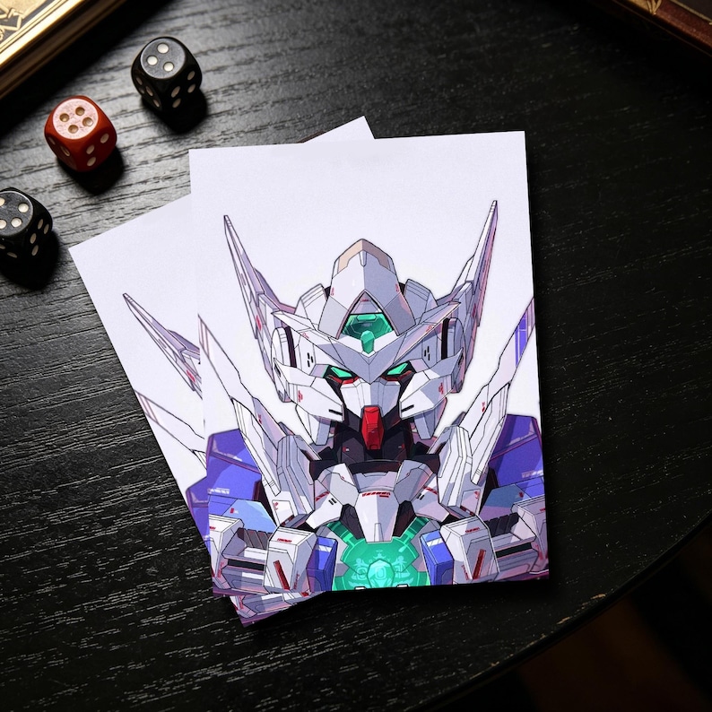 Op de afbeelding: Twee witte kaarten met een gedetailleerde illustratie van een Gundam-robot. De robot is overwegend wit met blauwe en rode accenten en een groene kern. Dobbelstenen liggen verspreid rond de kaarten op een zwart oppervlak.