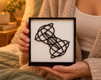 Può includere: Una cornice nera quadrata contenente uno sfondo bianco con una scultura geometrica astratta nera in tre dimensioni, caratterizzata da linee curve e anelli che si intersecano creando un motivo complesso, simmetrico e interconnesso.