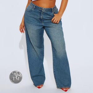 May include: High-waisted blue denim jeans with a wide-leg silhouette, featuring a classic five-pocket design, a button and zipper fly closure, and a medium wash finish. The jeans have a relaxed fit through the legs and a structured waistband.
