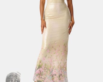 Può includere: Un abito lungo senza maniche color champagne ricoperto di paillettes scintillanti. Il vestito presenta un corpetto aderente con scollo a V e una stampa floreale sfumata nei toni del rosa e del verde lungo la parte inferiore della gonna.