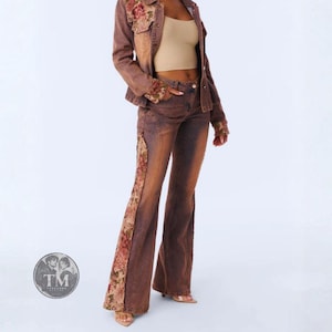 May include: A brown denim jacket and matching flared jeans set featuring floral fabric panels on the shoulders, cuffs, and down the sides of the legs. The outfit is paired with a beige sleeveless top. A circular logo with the text TM is visible.
