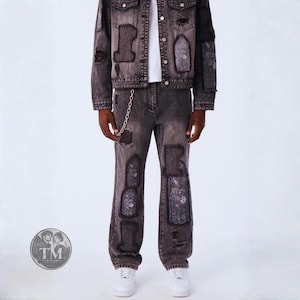 Könnte beinhalten: Ein Set aus anthrazitfarbener Jeansjacke und passender Jeans mit abgenutzten Flicken, ausgefransten Kanten und dunklen Stoffeinsätzen mit Muster. Die Jeans hat eine silberne Metallkette an der Gürtelschlaufe. Darunter wird ein weißes Oberteil getragen.
