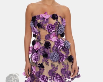 Può includere: Un abito corto senza spalline con una base in rete color carne decorata con applicazioni floreali tridimensionali viola, lavanda e nere. Il capo presenta un intricato ricamo viola e un orlo smerlato con un logo TM visibile in filigrana.