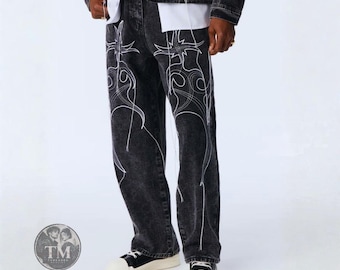 Può includere: Jeans in denim nero lavato all'acido con motivi a linee ricamate bianche in stile tribale sulla parte anteriore delle gambe. I pantaloni hanno un taglio dritto e sono abbinati a una giacca di jeans nera coordinata e scarpe da ginnastica.