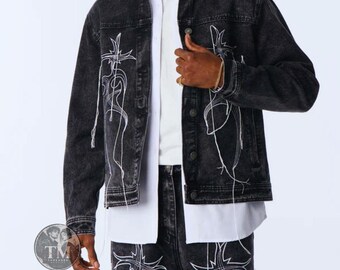 Può includere: Una giacca in denim nero lavaggio acido con un design a linee ricamate bianche in stile tribale sui pannelli frontali. La giacca presenta un colletto classico, maniche lunghe con polsini abbottonati e una chiusura frontale con bottoni.