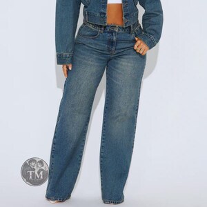 May include: A pair of medium-wash blue denim jeans with a high-waisted fit and wide-leg silhouette, paired with a matching cropped denim jacket. The ensemble features classic stitching, a button-fly closure, and a circular logo watermark in the corner.