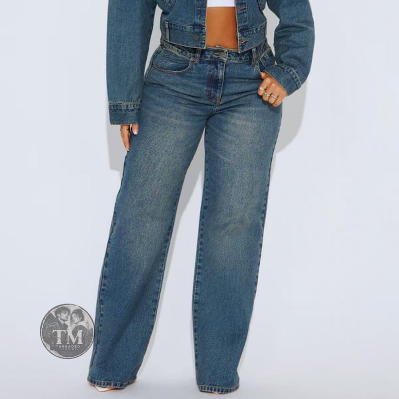 May include: A pair of medium-wash blue denim jeans with a high-waisted fit and wide-leg silhouette, paired with a matching cropped denim jacket. The ensemble features classic stitching, a button-fly closure, and a circular logo watermark in the corner.