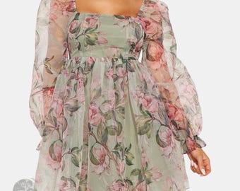 Può includere: Un abito corto con maniche lunghe a sbuffo e scollo quadrato, caratterizzato da una base color verde chiaro con un motivo floreale di fiori rosa e foglie verdi. Il capo è realizzato in un tessuto leggero e trasparente con gonna arricciata.