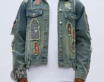 Può includere: Una giacca in denim azzurro con zone usurate e molteplici toppe rettangolari con motivi floreali e ornamentali. La giacca presenta una chiusura frontale con bottoni, due tasche sul petto con patta e maniche lunghe. Sotto è indossata una t-shirt bianca semplice.