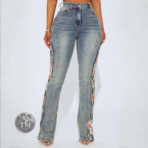 Può includere: Jeans in denim blu a vita alta con taglio a gamba dritta e un pannello verticale in pizzo floreale lungo la cucitura esterna di ogni gamba. Il denim presenta un lavaggio chiaro con cuciture visibili e una classica chiusura a zip.