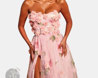 Può includere: Un abito lungo senza spalline color rosa chiaro con scollo a cuore e un alto spacco sulla gamba. Il corpetto e la gonna sono decorati con fiori in tessuto tridimensionali e una stampa floreale su un tessuto di tulle trasparente.