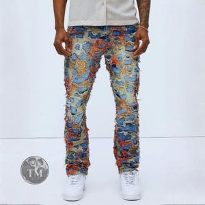 May include: Distressed blue denim jeans featuring a heavy patchwork design with frayed edges and vibrant orange, yellow, and red fabric accents throughout the legs. The pants have a slim fit silhouette and are paired with white sneakers.