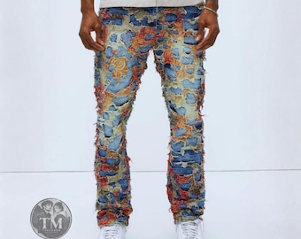 Può includere: Jeans in denim blu invecchiato con un fitto design patchwork, bordi sfilacciati e vivaci accenti di tessuto arancione, giallo e rosso lungo le gambe. I pantaloni hanno una vestibilità aderente e sono abbinati a scarpe da ginnastica bianche.