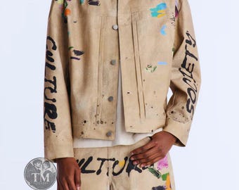 May include: A tan denim jacket and matching shorts set featuring a paint-splattered design in blue, green, orange, and purple. The jacket sleeves display the word CULTURE on the right and SOCIETY on the left in black, with CULTURE on the shorts.