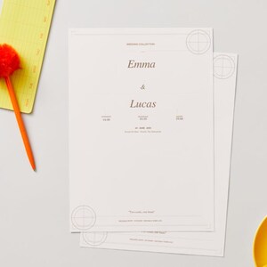 May include: A stack of wedding invitation cards with the names "Emma & Lucas" printed in brown. A bright orange pen with a fluffy pom-pom sits next to a yellow notepad. A yellow teacup is in the bottom right corner.