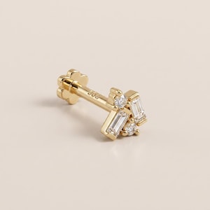 May include: A gold flat back stud earring featuring a cluster design with two baguette-cut clear stones and two round brilliant-cut clear stones. The post is marked with 585 and ends in a flower-shaped backing, crafted from polished yellow gold.