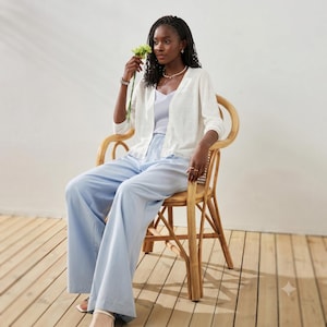 May include: A light blue camisole top paired with matching wide-leg trousers and a white open-front cardigan. The outfit is worn with a delicate silver necklace and a silver watch, creating a coordinated ensemble with soft pastel tones.