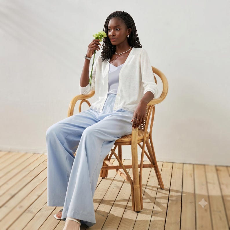 May include: A light blue camisole top paired with matching wide-leg trousers and a white open-front cardigan. The outfit is worn with a delicate silver necklace and a silver watch, creating a coordinated ensemble with soft pastel tones.