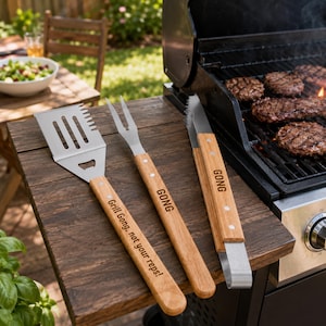 May include: A set of three stainless steel grilling tools with light wood handles. The spatula features a serrated edge and bottle opener, engraved with "Grill Gong, not your reps!". The fork and tongs are each engraved with the word "GONG".