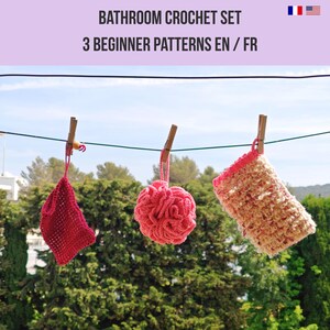 May include: A bathroom crochet set with three handmade items hanging on a clothesline. The set includes a red washcloth, a pink loofah, and a beige and pink scrubby. The text "BATHROOM CROCHET SET" and "3 BEGINNER PATTERNS EN / FR" is at the top.