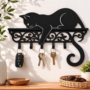 Pode incluir: Porta-chaves de metal preto com design de gato. O gato está deitado numa prateleira com volutas decorativas. Abaixo da prateleira, há ganchos para chaves. Várias chaves penduram dos ganchos. Um item decorativo e funcional.