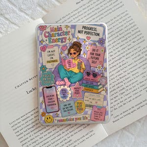 Puede incluir: Una funda transparente para teléfono con un diseño colorido que presenta una ilustración de dibujos animados de una persona leyendo, rodeada de frases e iconos motivacionales. La funda tiene un borde a cuadros morado y blanco.