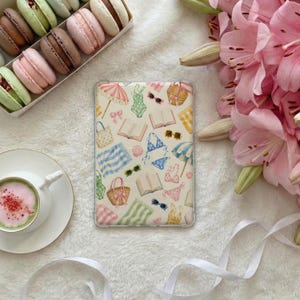 May include: A rectangular tablet case featuring a repeating pattern of summer-themed illustrations including beach umbrellas, swimsuits, sunglasses, straw bags, open books, and towels in soft pastel colors against a white background.
