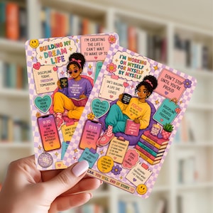 May include: Two illustrated cards with motivational quotes and images of a woman reading and drinking coffee. The cards feature text like "Building My Dream Life" and "I'm Working on Myself". The color scheme includes purple, yellow, and teal.