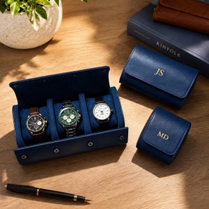May include: A navy blue leather watch roll containing three wristwatches, one with a brown strap and two with metal bands. Two additional navy blue leather watch cases are present, one embossed with JS and the other with MD, alongside a black pen.