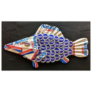 May include: A fish-shaped wall art piece constructed from Natural Light beer cans and bottle caps. The head and tail are fashioned from flattened aluminum can segments, while the body is covered in overlapping blue and silver bottle caps.