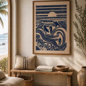 May include: A framed print depicts surfers in a blue and white linocut style. The artwork shows figures walking toward the ocean with surfboards, palm trees, and a setting sun. The print is displayed above a wooden bench with books and a bowl.