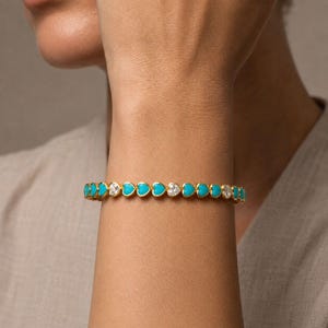 May include: A gold-toned bracelet featuring a repeating pattern of alternating bright turquoise heart-shaped links and clear, sparkling round-cut stones. The design consists of a continuous chain of these elements, creating a vibrant, symmetrical look.