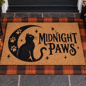 Peut inclure: Un paillasson rectangulaire en fibre de coco beige avec un motif noir représentant un chat assis dans un croissant de lune orné d'empreintes de pattes. Le texte MIDNIGHT PAWS est imprimé en noir avec de petites étoiles à quatre branches.