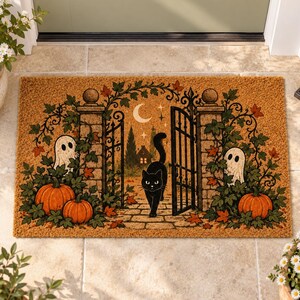 Peut inclure: Un paillasson rectangulaire en fibre de coco avec une illustration sur le thème d'Halloween représentant un chat noir marchant à travers un portail en fer forgé ouvert. Le décor inclut deux fantômes blancs, des citrouilles et du lierre.