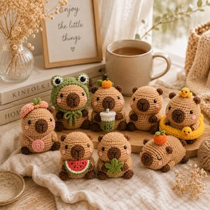 May include: A collection of nine small, tan, crocheted capybara figures. Each figure features unique accessories, including a frog hat, a watermelon slice, a boba tea cup, a yellow swim ring with two small ducks, and various fruit or leaf headpieces.