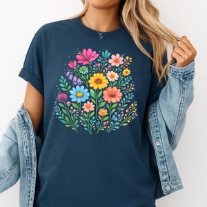May include: Navy blue t-shirt featuring a vibrant floral design. The graphic showcases a bouquet of colorful flowers, including pink, yellow, orange, and blue blooms, surrounded by green foliage. The shirt has rolled-up sleeves and a relaxed fit.
