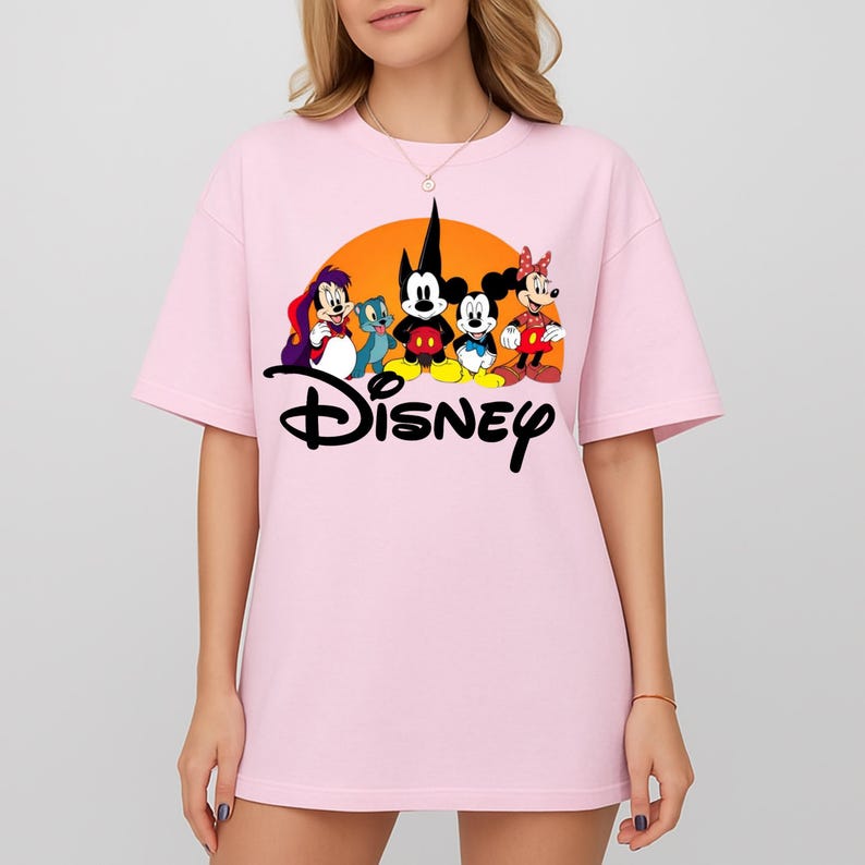 Pu&ograve; includere: T-shirt rosa chiaro con grafica Disney. La grafica include Topolino, Minnie e altri personaggi Disney davanti a un sole arancione. La parola "Disney" &egrave; scritta in nero sotto i personaggi.
