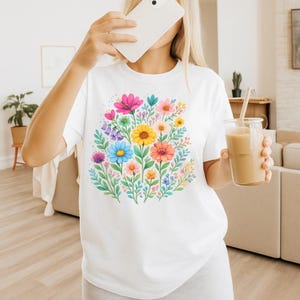 May include: White t-shirt featuring a vibrant floral design. The graphic showcases a bouquet of colorful flowers, including pink, yellow, blue, and orange blooms, surrounded by green leaves. The shirt is a casual, everyday wear item.