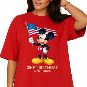 Puede incluir: Camiseta roja con Mickey Mouse sosteniendo una bandera estadounidense. Mickey lleva pantalones cortos rojos, guantes blancos y zapatos amarillos. El texto "250TH BIRTHDAY 1776-2026" est&aacute; impreso debajo.